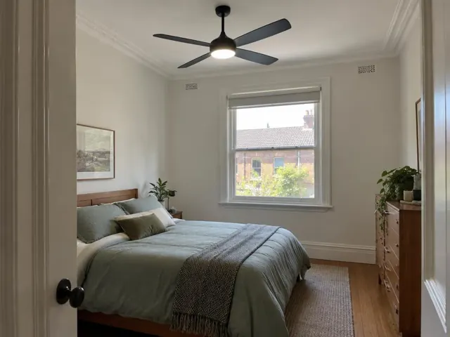 Bedroom with a black ceiling fan and light on a white plaster ceiling above a bed in Lilyfield