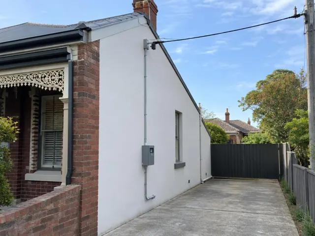 White rendered house wall with overhead service cable and point-of-attachment bracket in Annandale